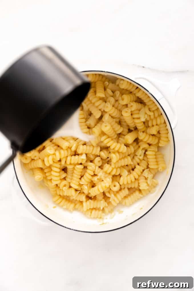 Zesty Lemon Garlic Pasta 7 A measuring cup carefully pouring starchy pasta water into a pot of pasta, initiating the sauce creation