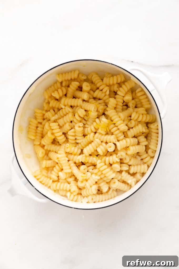 Zesty Lemon Garlic Pasta 8 Lemon fusilli pasta being tossed in a white pot, with the sauce beginning to emulsify and coat the noodles