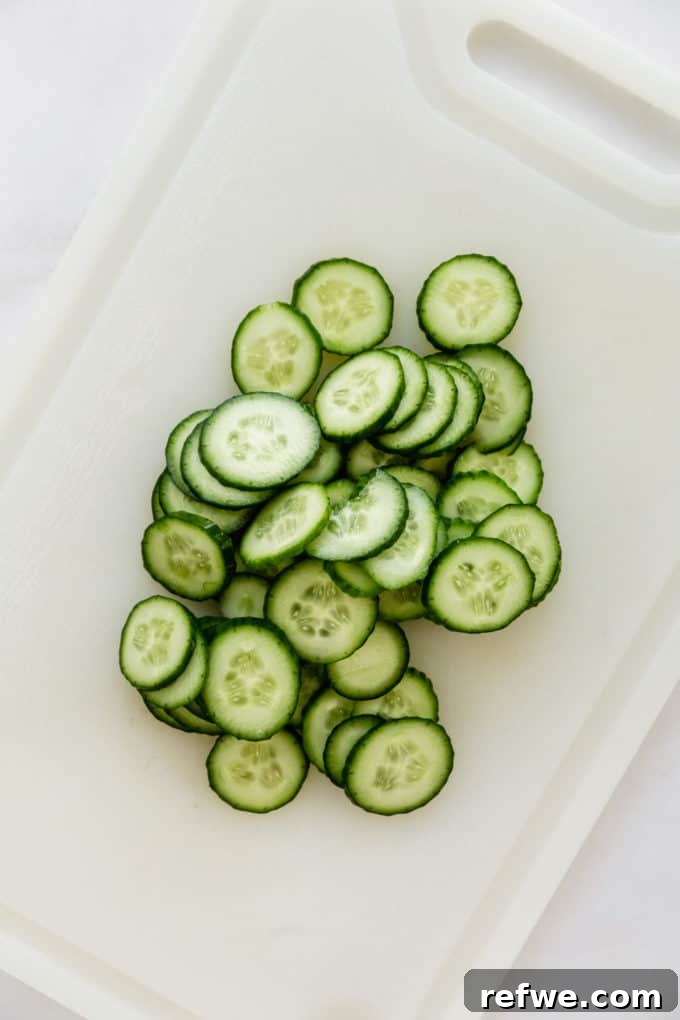 Neatly arranged, thinly sliced cucumbers fanned out on a pristine white cutting board, showcasing their uniform shape and freshness.