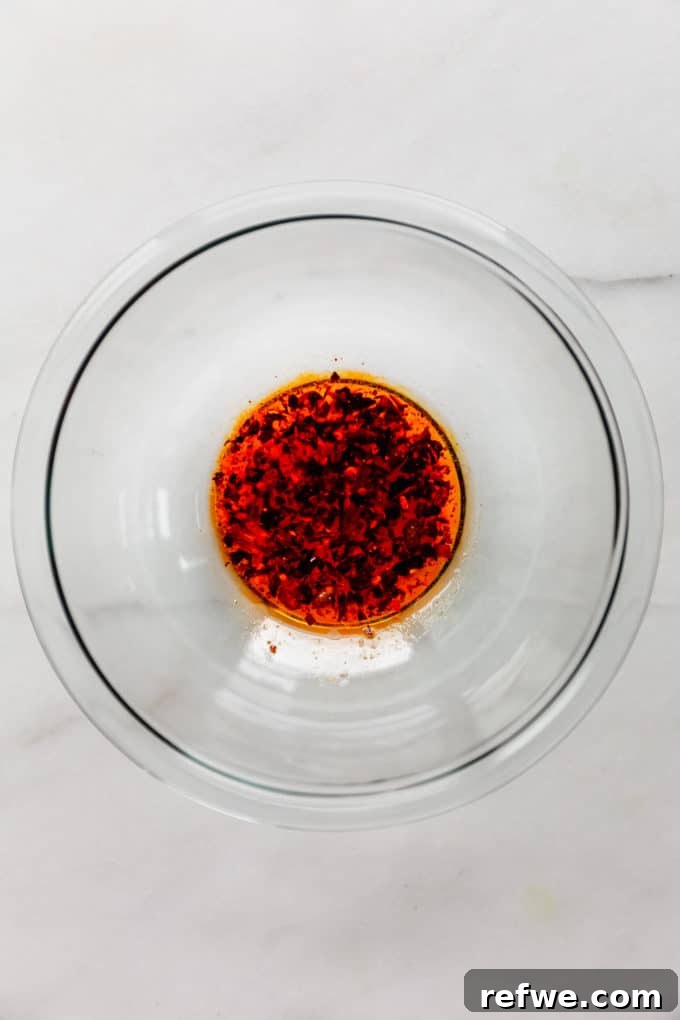A clear glass mixing bowl filled with a perfectly emulsified Asian dressing, showcasing its rich amber color before the addition of other ingredients.
