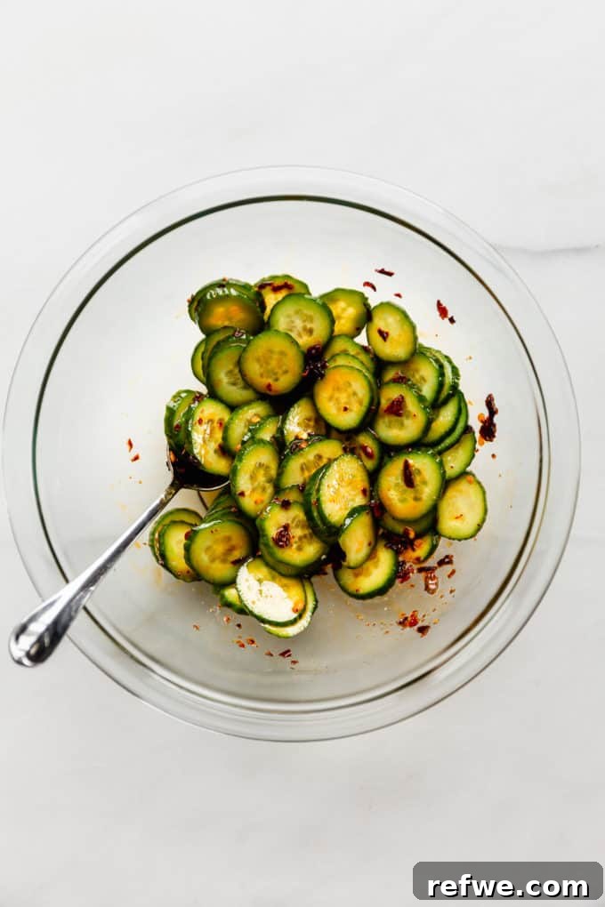 A mixing bowl brimming with freshly prepared Asian cucumber salad, showcasing the vibrant green slices coated in dressing, ready for its final touches.