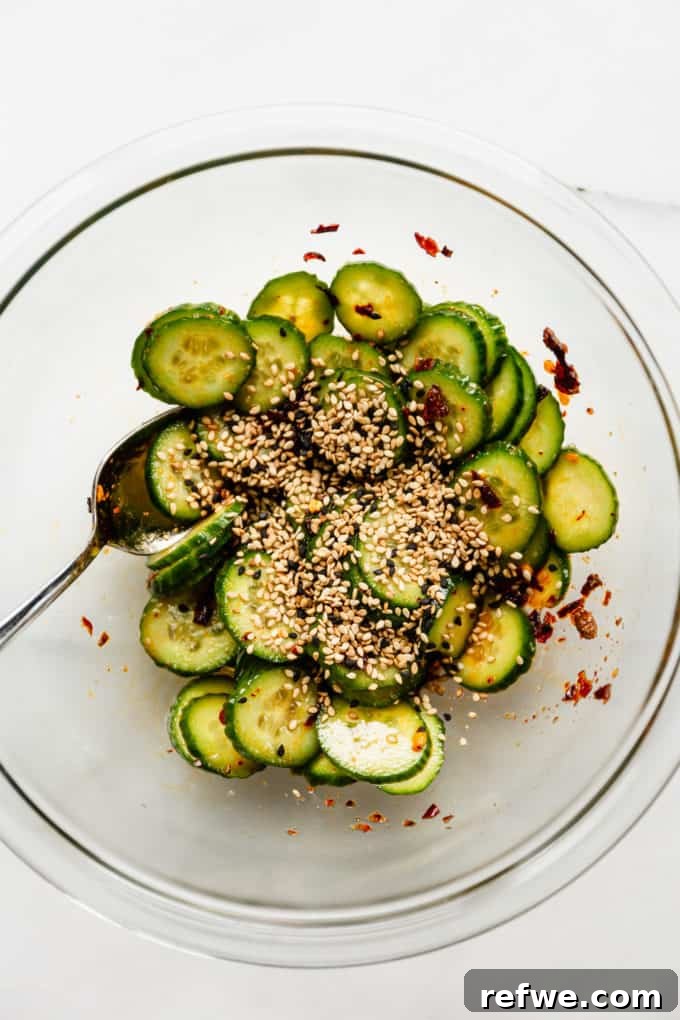 The finished Asian cucumber salad, beautifully presented in a mixing bowl and generously topped with toasted sesame seeds, ready to be savored.