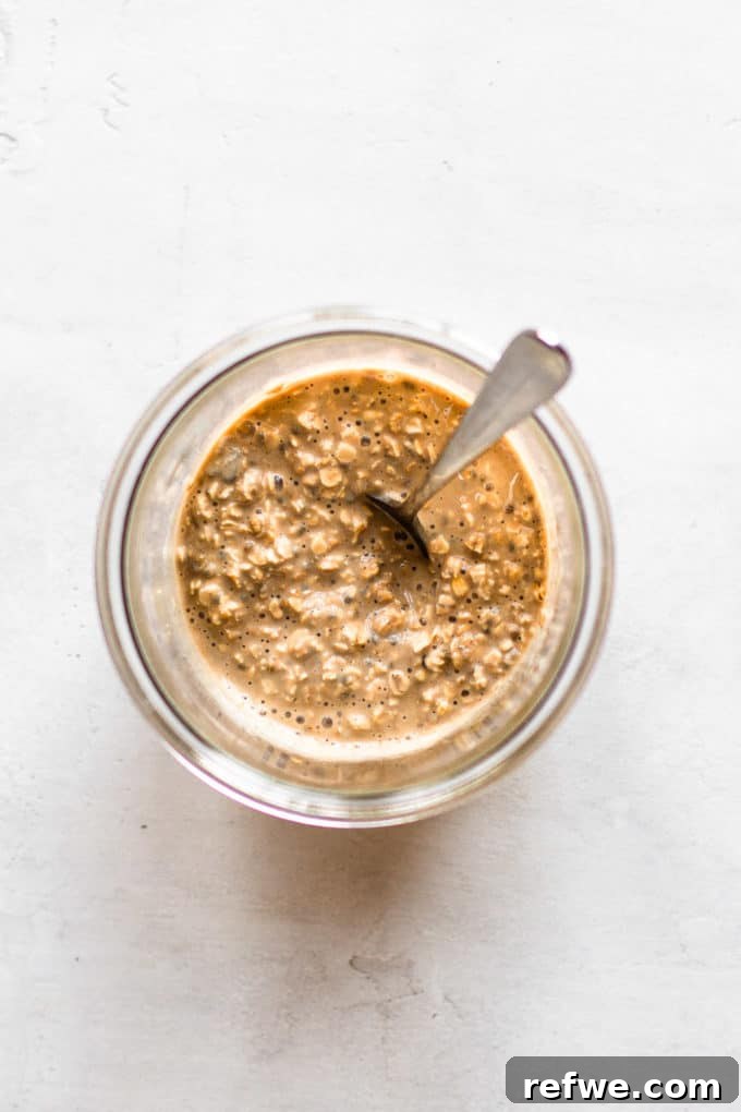 Java Overnight Oats 7 A spoon resting in a cup of overnight oats, milk, and coffee, highlighting the creamy texture and rich color of the blend.