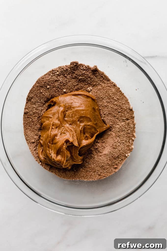 Effortless Fudgy Chocolate Protein Bars 6 Almond butter being added to a bowl of dry ingredients, signaling the start of the dough-making process.