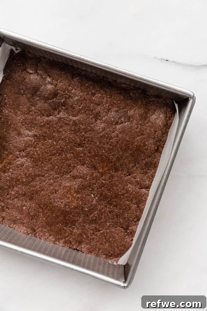 Effortless Fudgy Chocolate Protein Bars 8 Chocolate protein bar dough perfectly pressed into an 8x8 inch pan lined with parchment paper, forming a smooth, compact base.