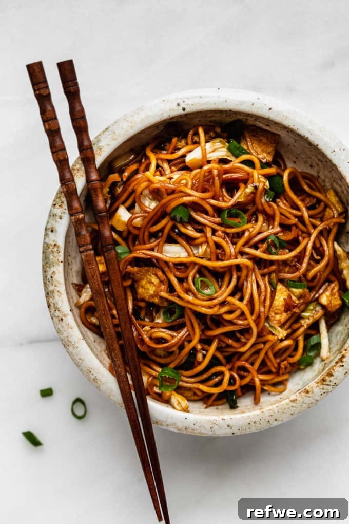 Indonesian Fried Noodles Mie Goreng 2 A vibrant bowl of Mie Goreng noodles garnished with fresh scallions and chili, ready to be enjoyed with chopsticks.