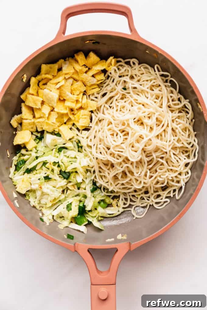 Indonesian Fried Noodles Mie Goreng 11 Sautéed vegetables, cooked noodles, and omelette pieces combined in a pink pan.