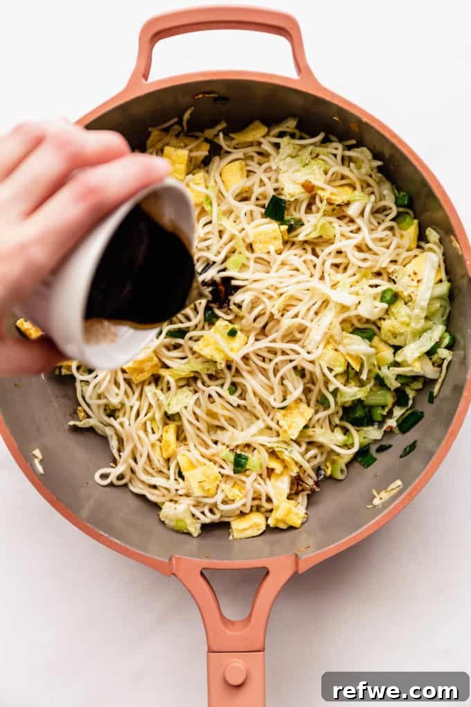 Indonesian Fried Noodles Mie Goreng 12 Stir-fry sauce being poured over a pan of noodles and vegetables.