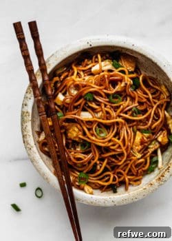 A vibrant bowl of Mie Goreng noodles garnished with fresh scallions and chili, ready to be enjoyed with chopsticks.