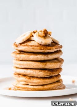A stack of 6 oat flour pancakes with bananas and walnuts on top