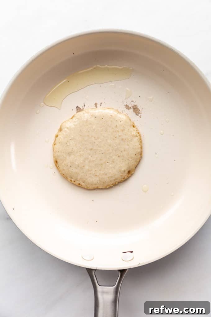 Wholesome Oat Flapjack Feast 9 An uncooked oat flour pancake on a hot white pan, showing early signs of cooking