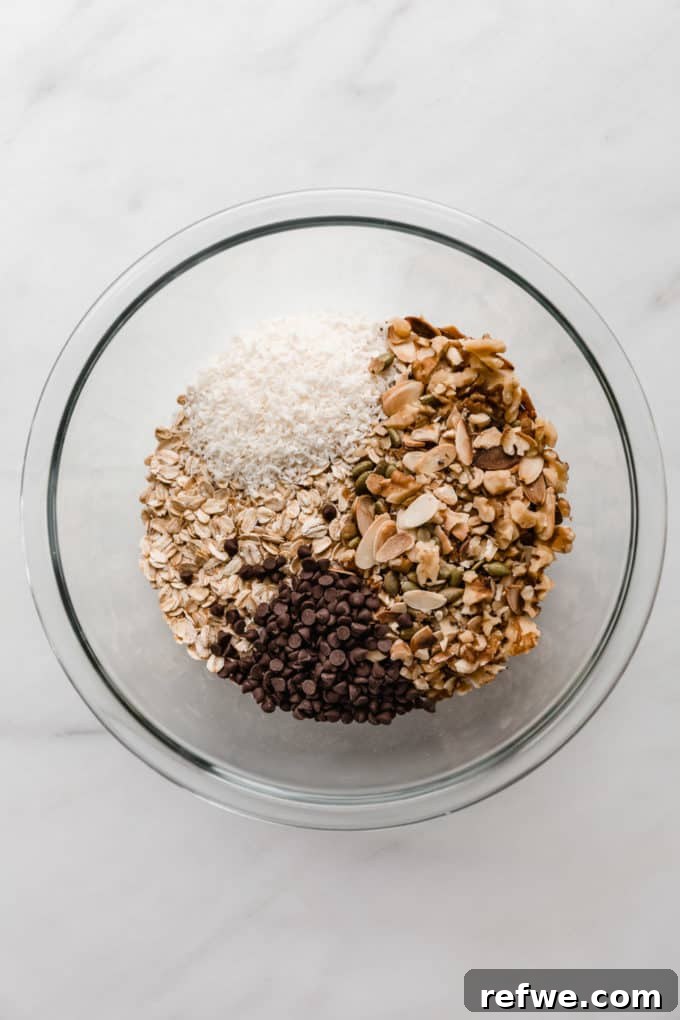 Wholesome Energy Muesli Bars 3 A vibrant mix of oats, nuts, coconut, and mini chocolate chips in a large mixing bowl, ready for the next step.