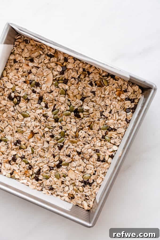 Wholesome Energy Muesli Bars 7 Unbaked muesli bar mixture firmly pressed into a square baking pan lined with parchment paper.