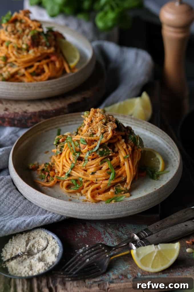 31 Irresistible Vegan Pasta Dishes 22 A vibrant plate of spaghetti infused with harissa, accompanied by a fresh lemon wedge on a wood table.