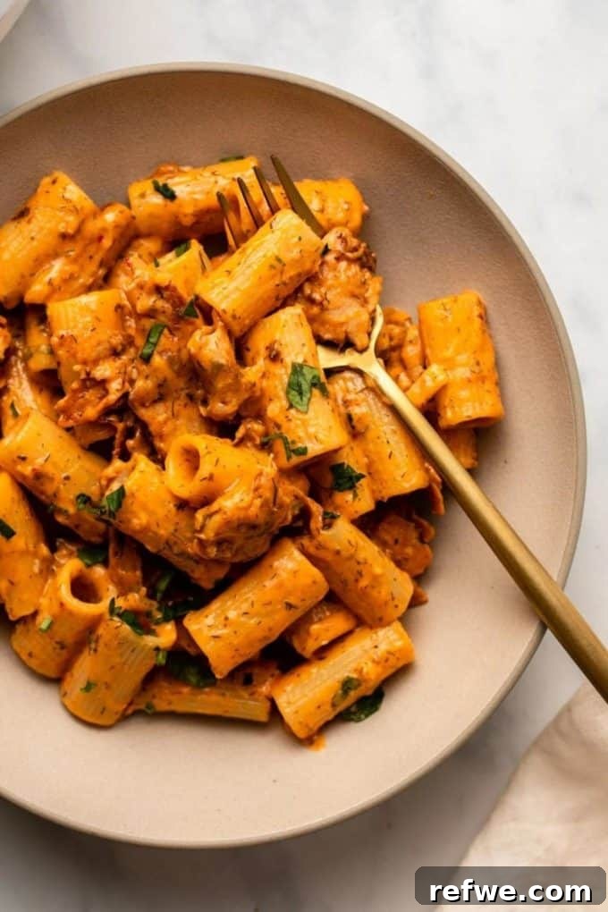 31 Irresistible Vegan Pasta Dishes 5 Rigatoni pasta coated in a creamy red buffalo ranch sauce, presented on a stylish pink plate with a gold fork.