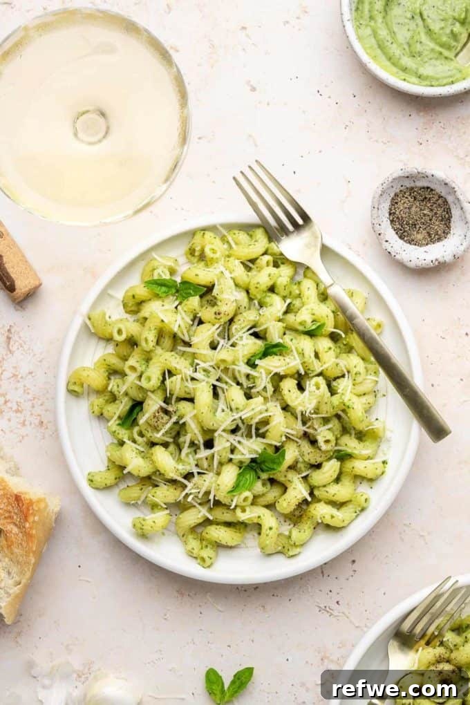 31 Irresistible Vegan Pasta Dishes 15 A pristine white plate showcasing vibrant avocado pesto pasta, beautifully garnished with fresh basil leaves.