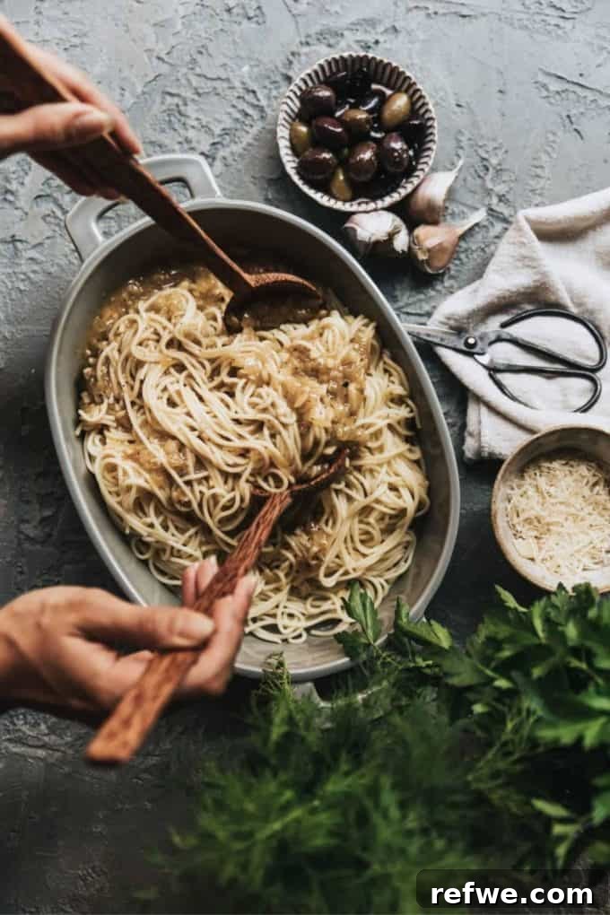 31 Irresistible Vegan Pasta Dishes 16 Spaghetti elegantly arranged in a grey baking dish, accompanied by a side of olives and fresh garlic cloves.