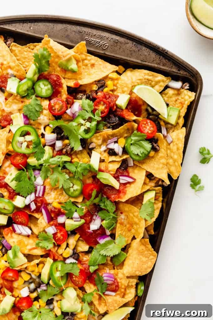 Irresistible Vegetarian Nachos 2 Crispy tortilla chips piled high with melted cheese, black beans, corn, diced avocado, fresh salsa, and cilantro on a baking sheet, ready to be enjoyed.