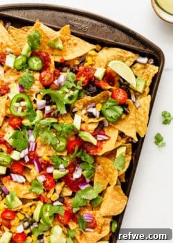 nachos topped with avocado, salsa and cilantro on a baking sheet