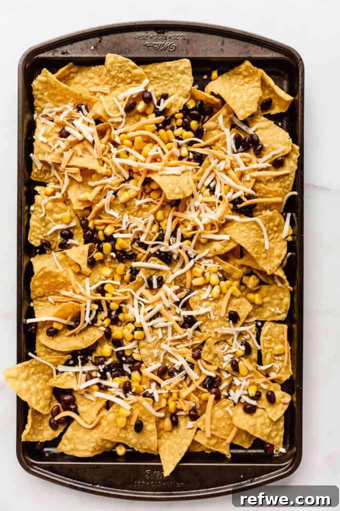 Irresistible Vegetarian Nachos 4 The first layer of tortilla chips topped with black beans, corn, and shredded cheese on a baking sheet, ready for the next layer.