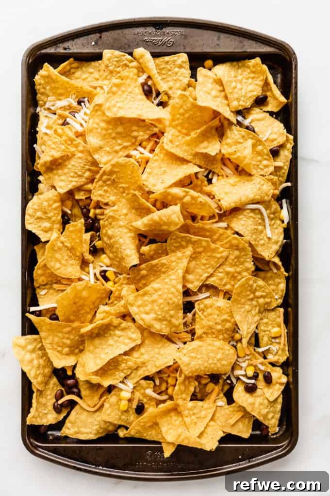 Irresistible Vegetarian Nachos 5 Two layers of tortilla chips, beans, corn, and cheese assembled on a baking sheet before baking.