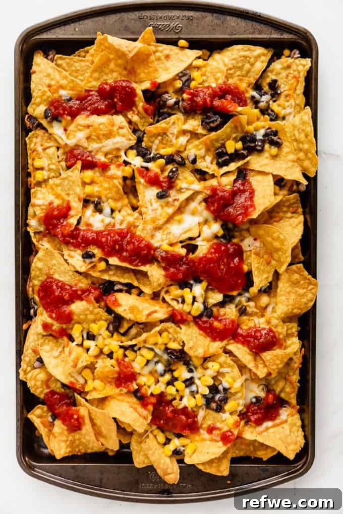 Irresistible Vegetarian Nachos 6 Freshly baked nachos with melted cheese and a generous topping of salsa on a baking sheet.