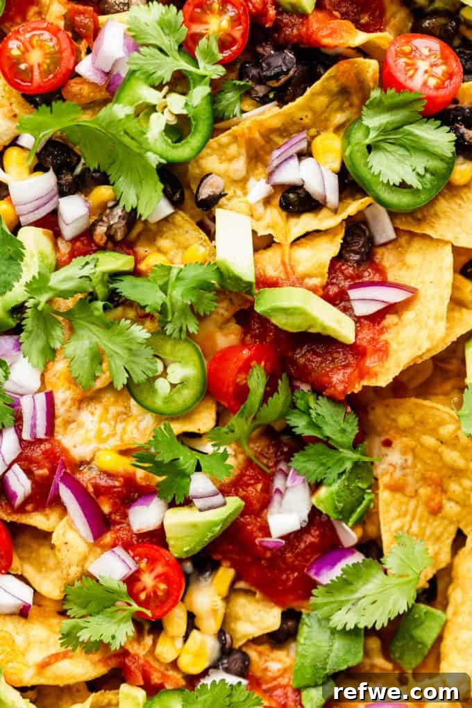 Irresistible Vegetarian Nachos 9 A vibrant close-up of a generous plate of vegetarian nachos, beautifully arranged with melted cheese, black beans, corn, diced fresh tomatoes, red onions, and a sprinkle of bright green cilantro.