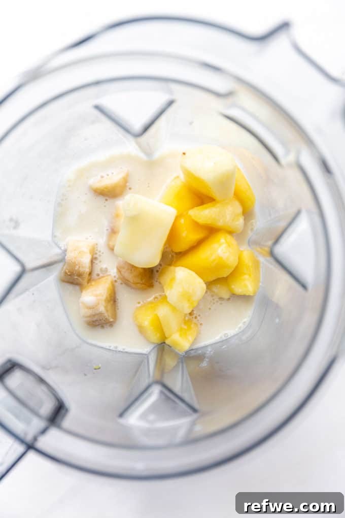 Pina Colada Dream Smoothie 4 Coconut milk, frozen pineapple chunks, and sliced frozen bananas being added to a high-speed blender.