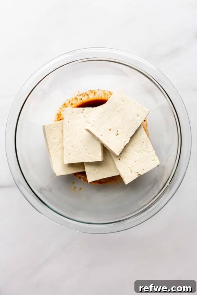 Slices of extra-firm tofu ready for marination in a clear bowl.