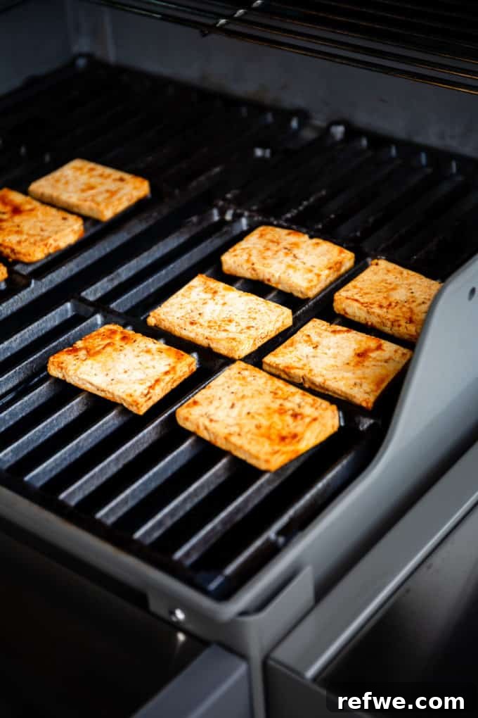 Marinated tofu cooking on a hot grill, showing early grill marks.