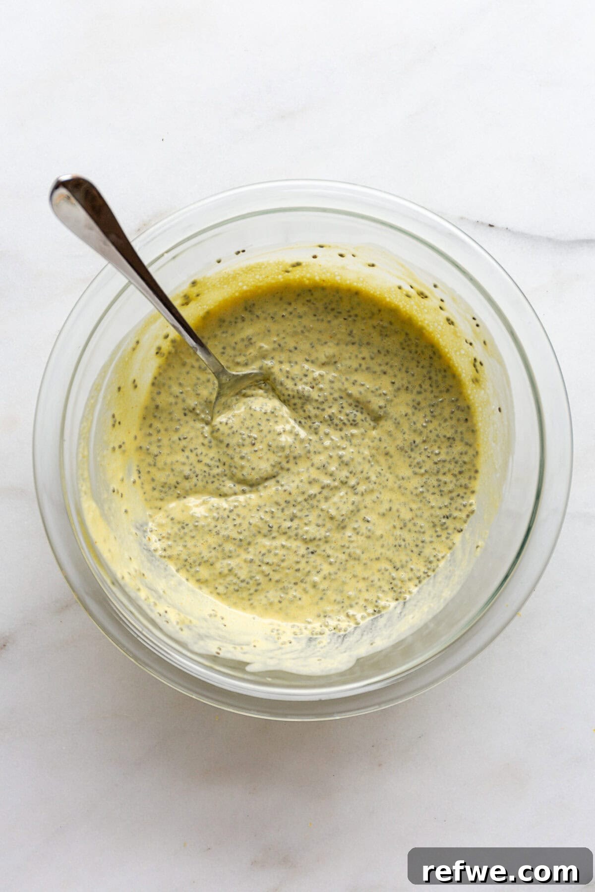 Sunshine Lemon Chia Pudding 8 Lemon chia pudding in a mixing bowl with a spoon, showing its initial consistency before chilling.
