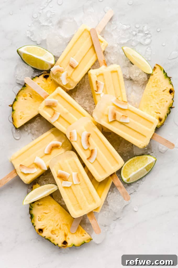 Paradise Pina Colada Pops 2 Pina Colada Popsicles on a marble counter topped with toasted coconut flakes, evoking a tropical summer vibe.