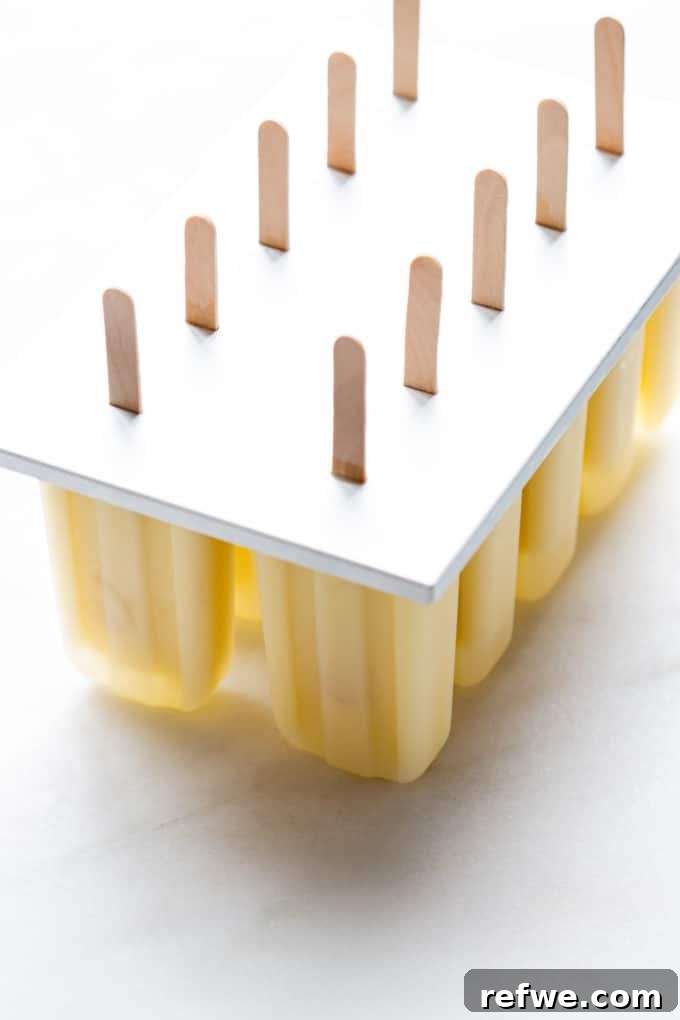 Paradise Pina Colada Pops 6 Pina Colada popsicle mixture poured into a popsicle mold with sticks inserted, ready for freezing.