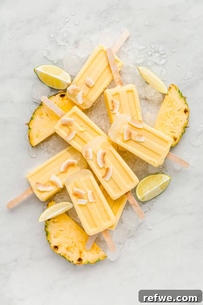 Paradise Pina Colada Pops 8 Collection of Pina Colada popsicles garnished with pineapple slices and lime wedges, presented on a rustic board, signifying a delightful summer dessert.