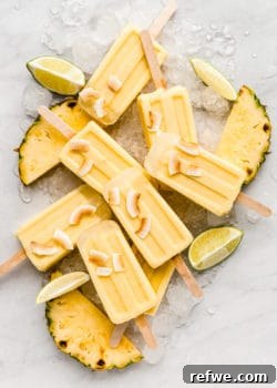 Pina Colada Popsicles on a marble counter topped with coconut flakes, symbolizing a refreshing treat.