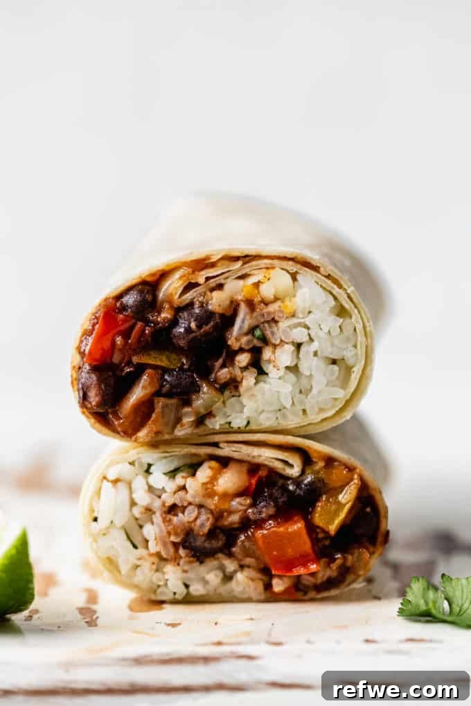 Two vibrant black bean veggie burritos, perfectly rolled and stacked on a rustic wooden board, ready to be enjoyed.