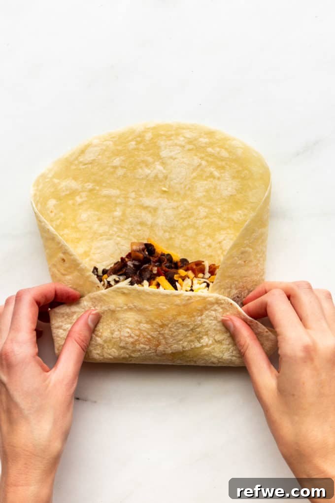 A partially rolled tortilla, showcasing the tightly tucked filling as it begins to take the shape of a burrito.