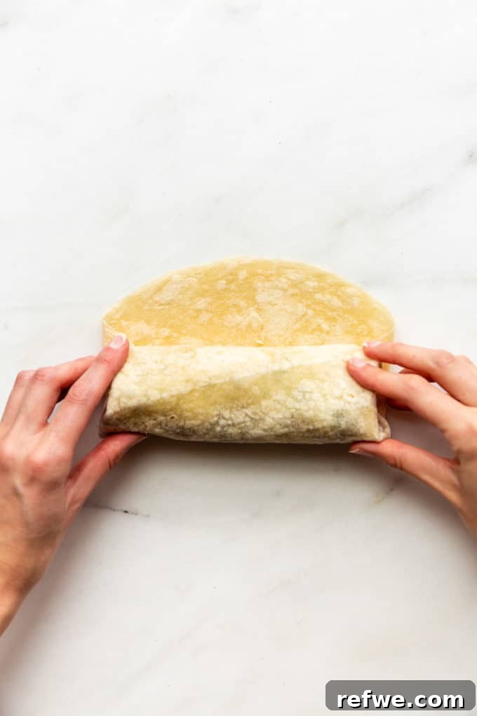 Hands demonstrating the final stages of rolling a tortilla into a perfectly cylindrical and secure burrito.