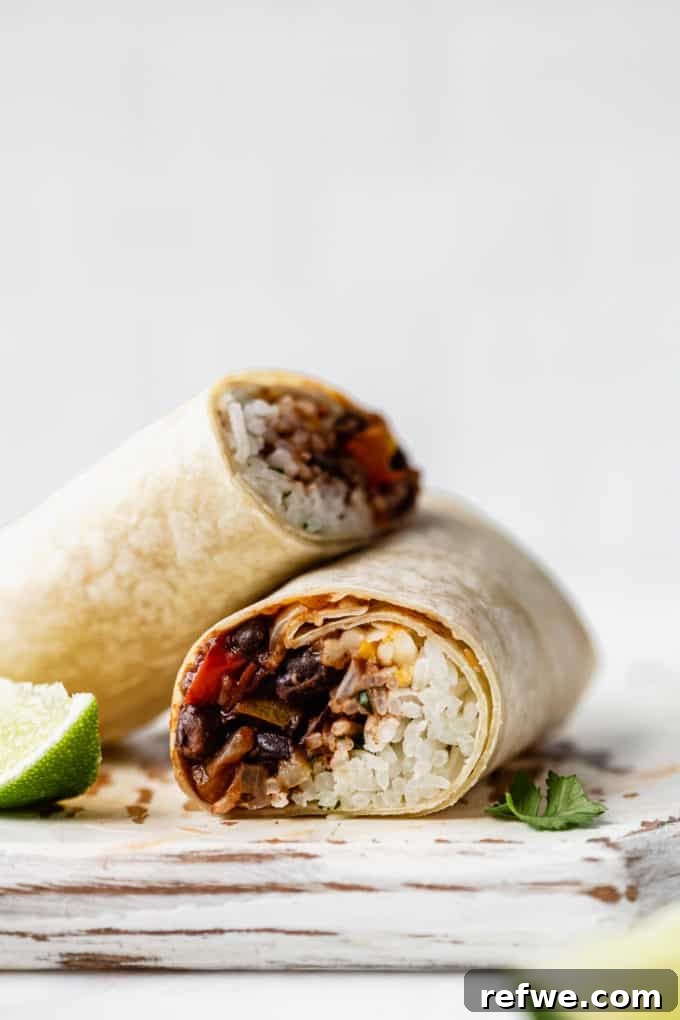 A freshly cut veggie burrito revealing its colorful layers of rice and black beans, garnished with a vibrant lime wedge and fresh cilantro.