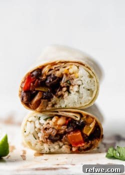 Two vibrant black bean veggie burritos, perfectly rolled and stacked on a rustic wooden board, ready to be enjoyed.