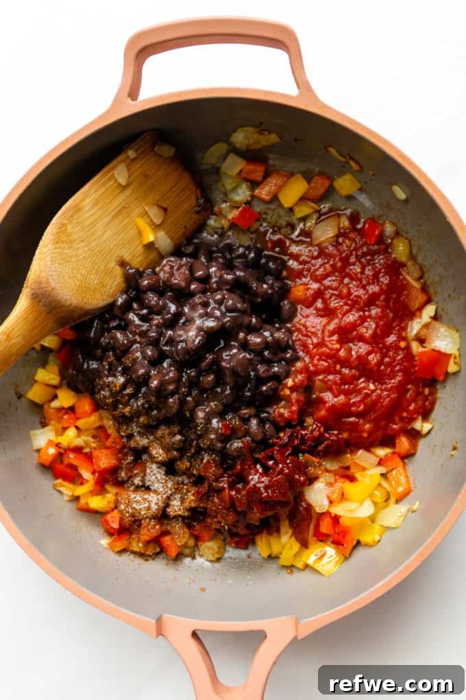 A vibrant mix of black beans, chunky salsa, colorful bell peppers, and smoky chipotle simmering in a pink skillet on the stove.