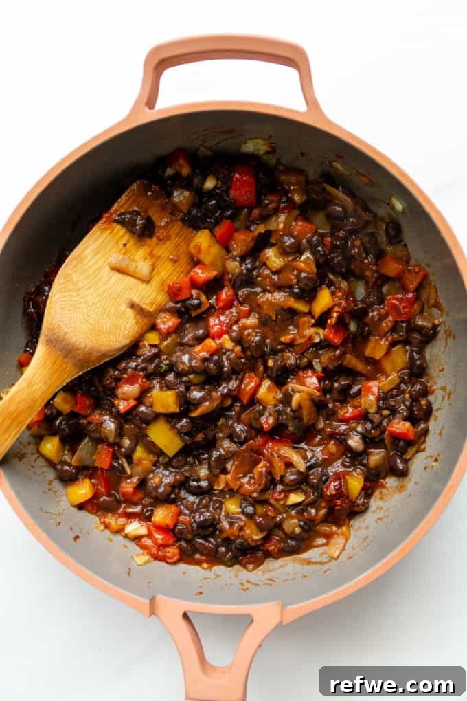 A close-up view of chipotle-infused black beans and bright bell peppers bubbling in a pink pan, creating a rich and aromatic filling.