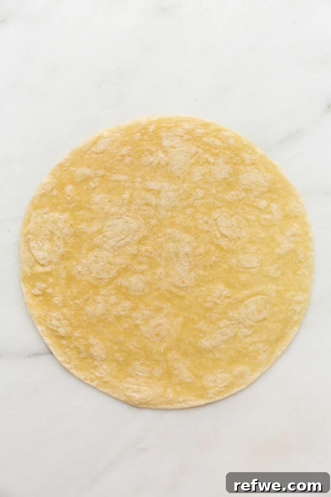 A large, soft tortilla laid flat on a pristine white marble cutting board, ready for filling.