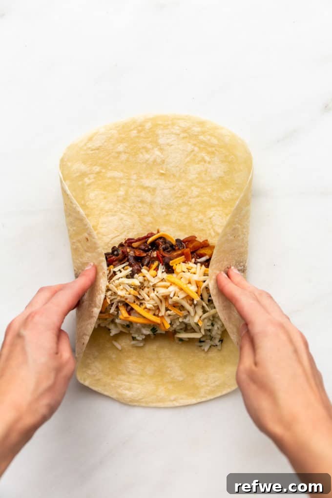 A hand expertly folding the side edges of a veggie burrito inwards, securing the filling before the final roll.