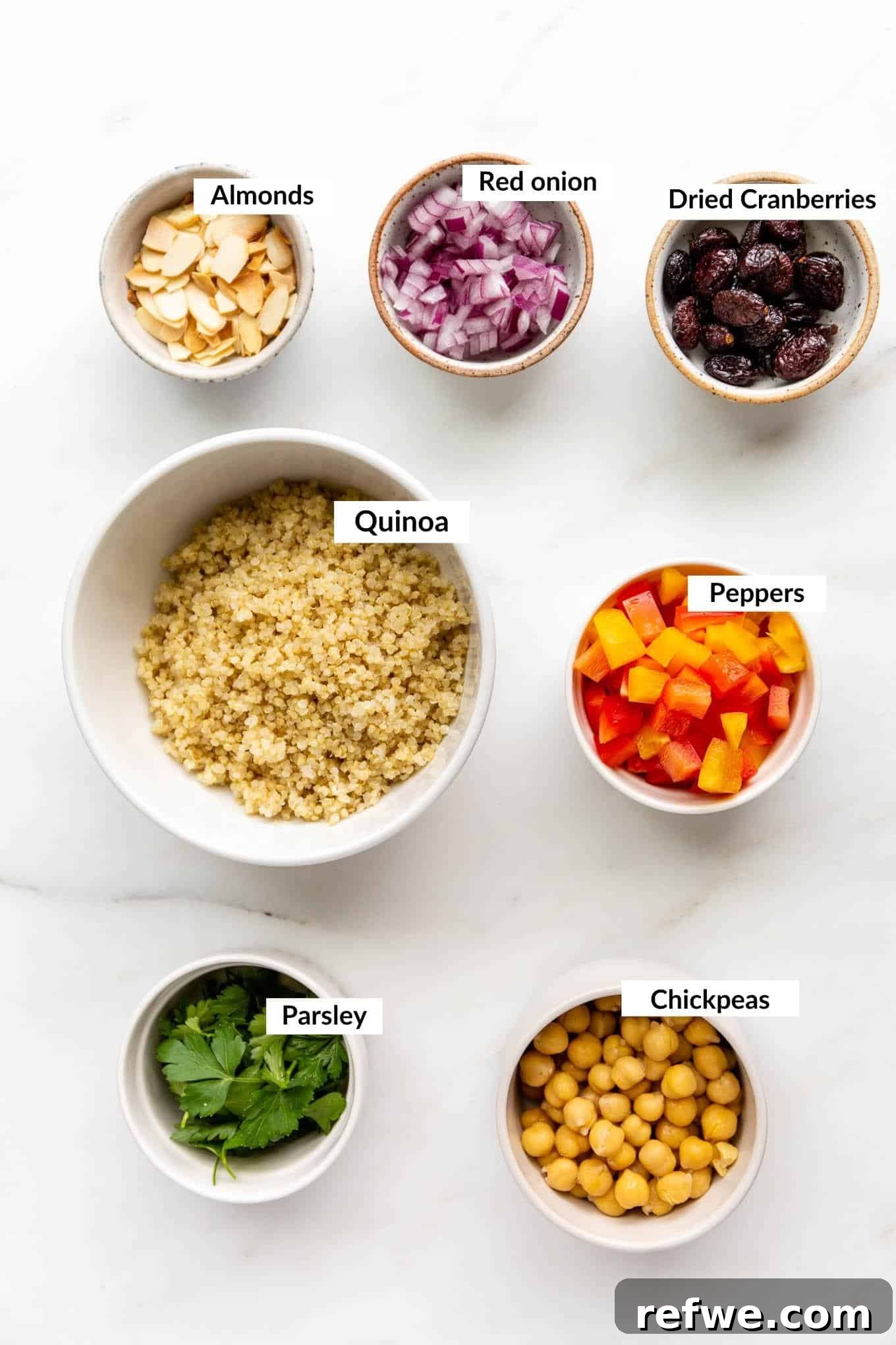 Close-up of fresh ingredients for quinoa chickpea salad including cooked quinoa, chickpeas, bell pepper, red onion, parsley, cranberries, and sliced almonds