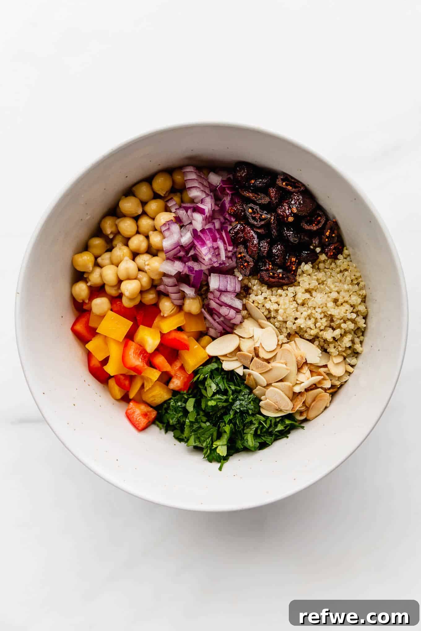 A large mixing bowl filled with cooked quinoa, chickpeas, chopped vegetables, dried cranberries, and sliced almonds, ready for dressing