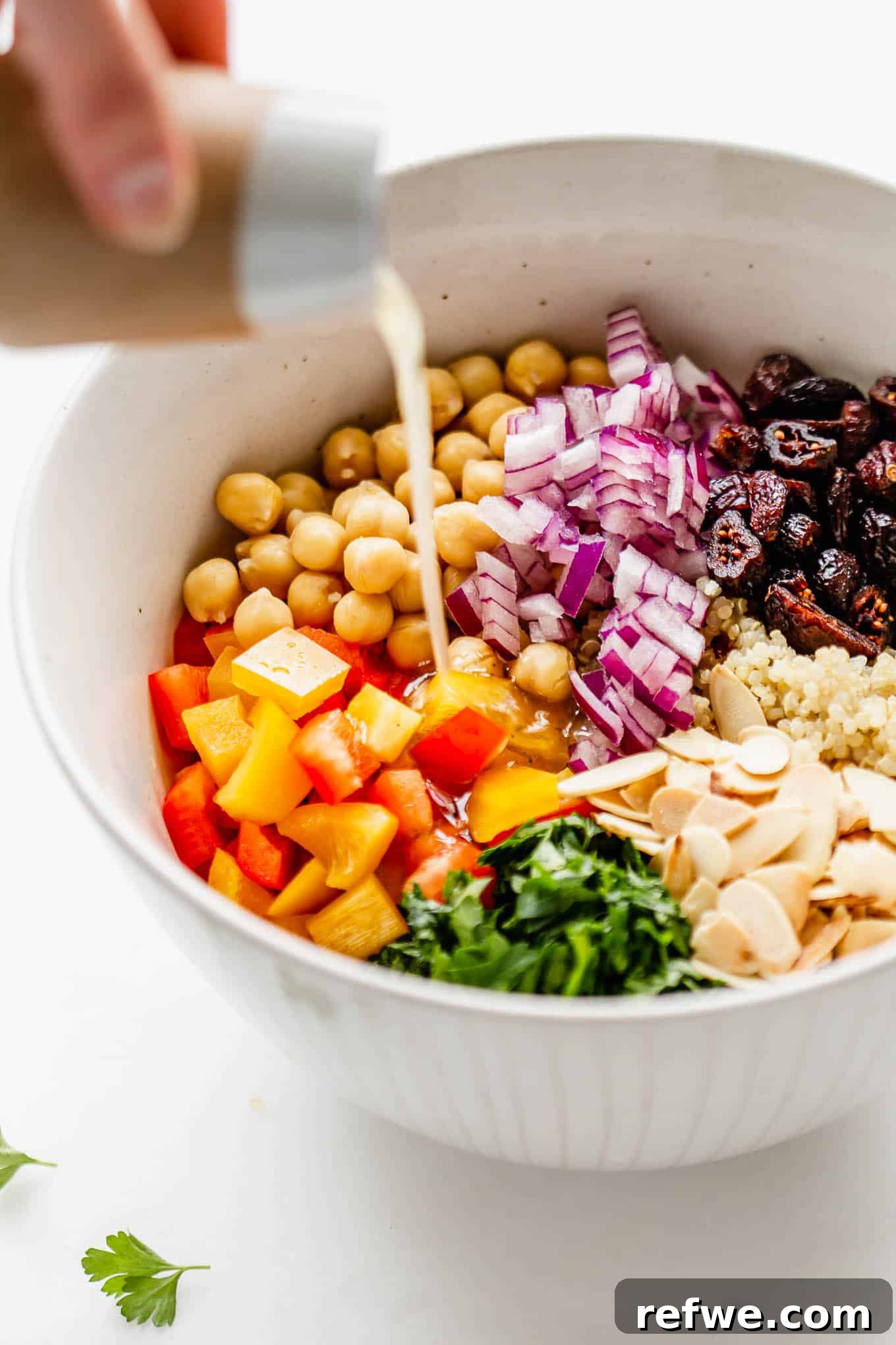 A small jar of lemon vinaigrette being poured over a bowl of quinoa chickpea salad