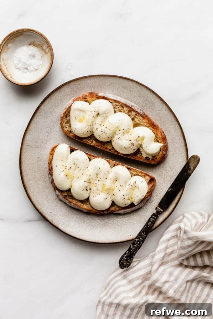 Pillowy Ricotta Toast 5 Two perfectly assembled slices of whipped ricotta toast on a plate, topped with olive oil.