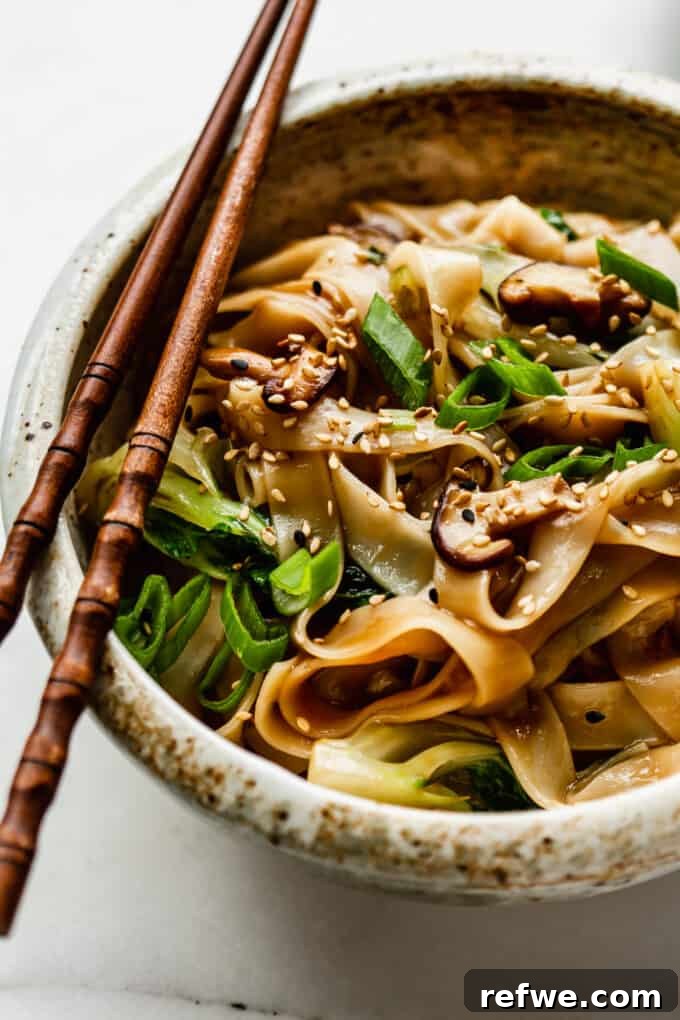 Wok-Tossed Ho Fun 12 A close-up of a rustic white ceramic bowl filled with perfectly cooked Ho Fun Noodles, garnished with fresh herbs and sesame seeds.