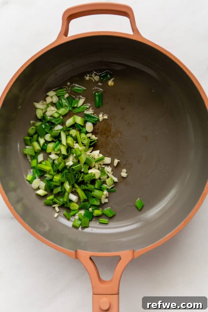 Wok-Tossed Ho Fun 4 Green onions and minced garlic sizzling in a hot pink pan, creating an aromatic base.
